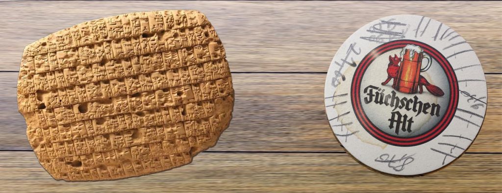 Eine Babylonische Keilschrifttafel als Beispiel für einen Babylon-Scheck liegt neben einem Bierdeckel, der ringsherum die Zählstriche der getrunkenen Biere zeigt.