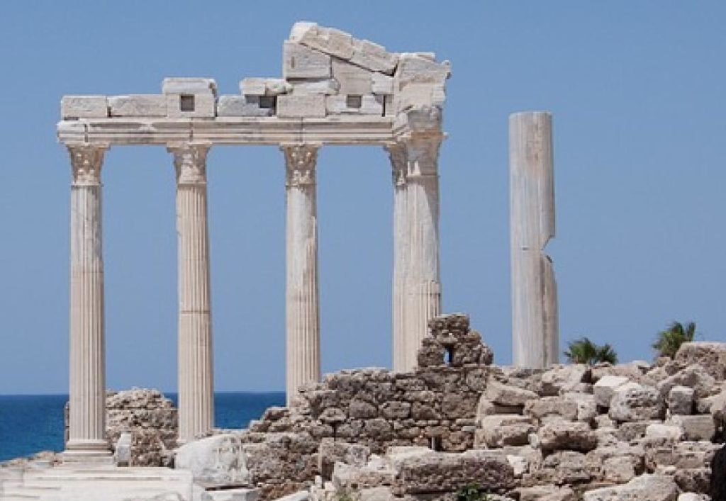Fünf antike Säulen vor Meereskulisse.